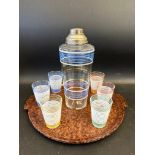 An Art Deco bakelite tray with a glass cocktail shaker and six matching beakers.