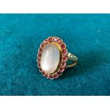 A moonstone and garnet ring, one oval cut white moonstone surrounded by 20 circular faceted cut