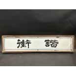 An enamel sign bearing Oriental letters, framed, 24 3/4 x 6".