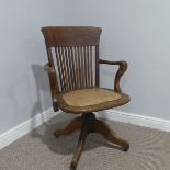 An Early 20thC oak swivel Desk Chair, shaped and rectangular stickback with swan armrests,