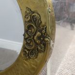 An Arts & Crafts oval brass mirror with decorative overlay to four of its edges, has it's original
