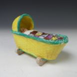 A 19thC Pearlware figure of a Baby in a Cradle, the green and yellow coloured cradle containing baby