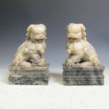 A pair of 20thC Chinese carved soapstone Dogs of Foo, modelled in typical pose, raised on plinth