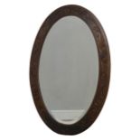 An Arts and Crafts carved oak wall Mirror, foliate scroll frame encasing bevelled plate, of large