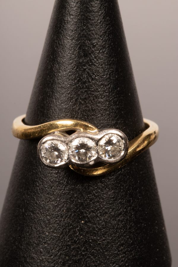 A diamond three-stone ring in an 18ct yellow gold crossover setting, the inner shank marked .