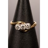 A diamond three-stone ring in an 18ct yellow gold crossover setting, the inner shank marked .