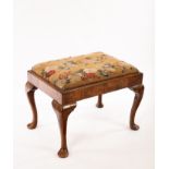 An 18th Century walnut stool with a needlework seat, on cabriole legs with pad feet,