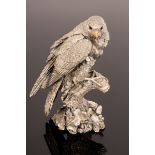 A filled silver model of a bird of prey, perched on a stump,