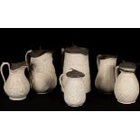 Six saltware jugs, various patterns, pewter lids,