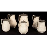 Six saltware jugs, various patterns, pewter lids,