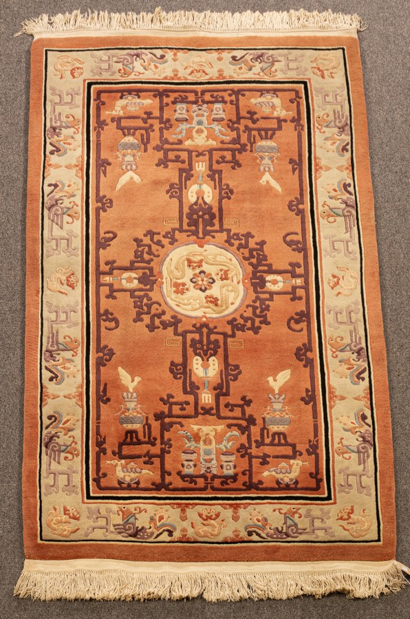 A Chinese superwash rug, the peach field with vases and centred by an ivory medallion of dragons,