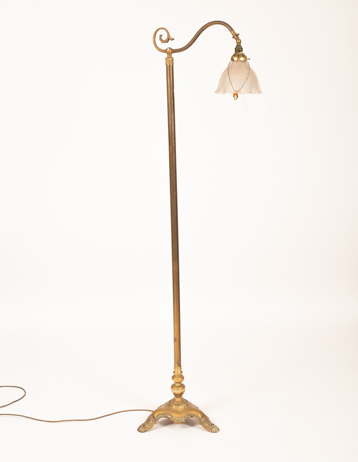 A brass standard lamp with clear flared glass shade on three claw feet,