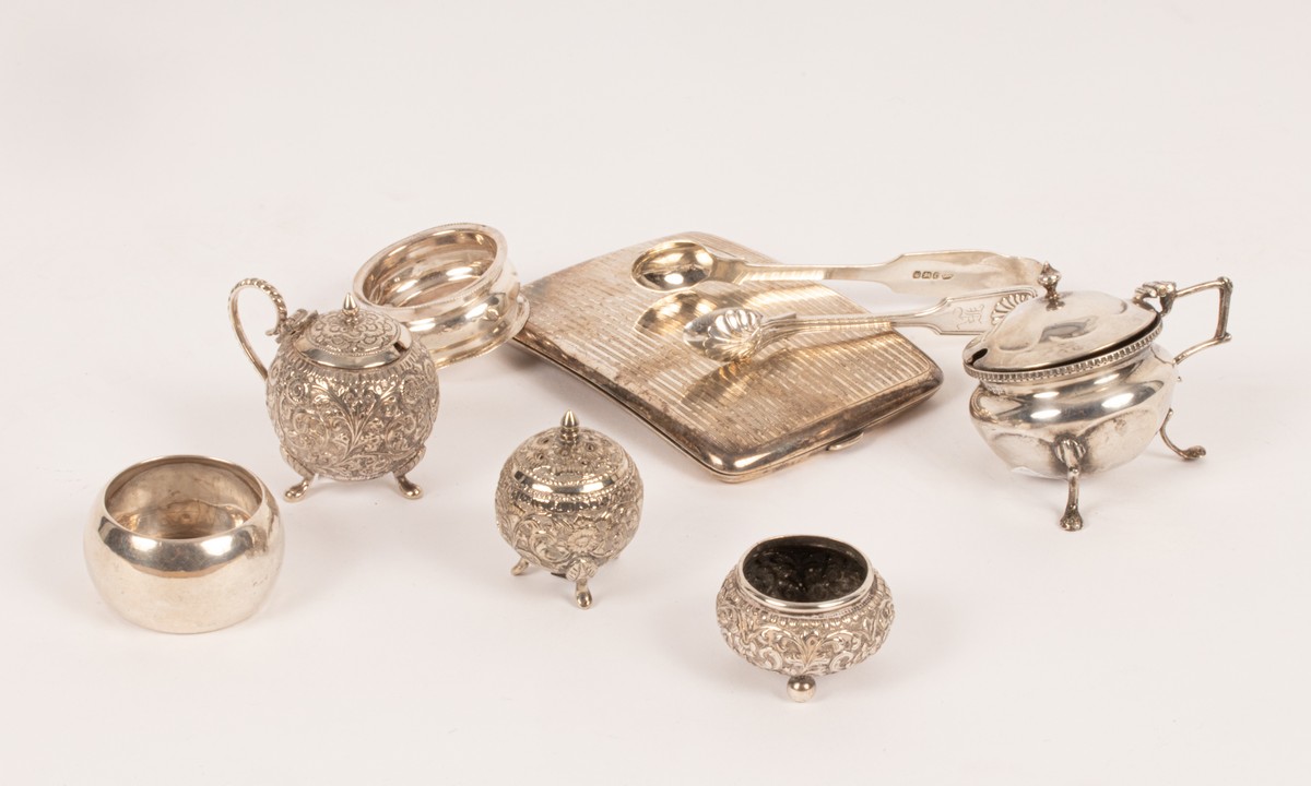A quantity of silver comprising two napkin rings, a cigarette case, an Indian three-piece cruet,