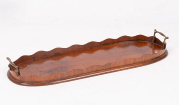 An oval mahogany tray with serrated border and brass handles,