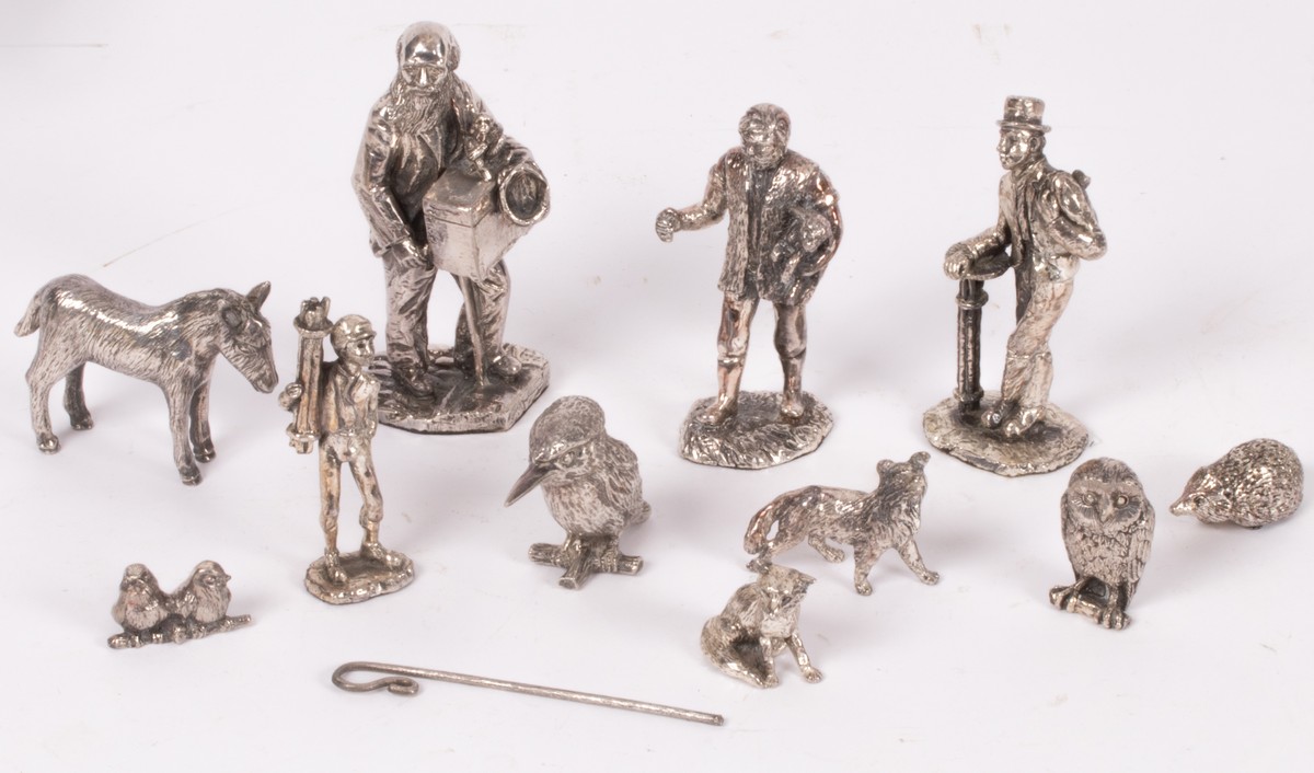 A group of white metal figures, including shepherd, chimney sweep, organ grinder, owl, donkey, etc.