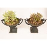 A pair of green cast iron garden urns with twin scroll handles on square plinths,