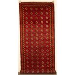 A Bokhara khelleh or long rug, Turkestan, strawberry red field of cruciform guls,
