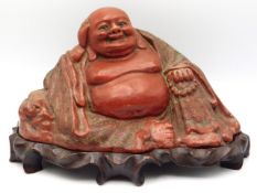 A c.1900 Chinese lacquerware laughing Buddha on carved hardwood organic plinth, marked "China" to un