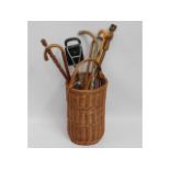 A wicker cane basket with contents including a shooting stick & six walking sticks/canes