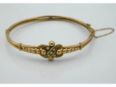 A yellow metal bangle set with pearl, tests electr