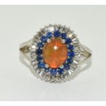 Orange opal surrounded with blue/clear stones set in silver ring Size U