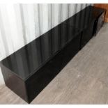 Pair of contemporary black two door low cupboards with smoked glass tops and shelving inside. 125cms