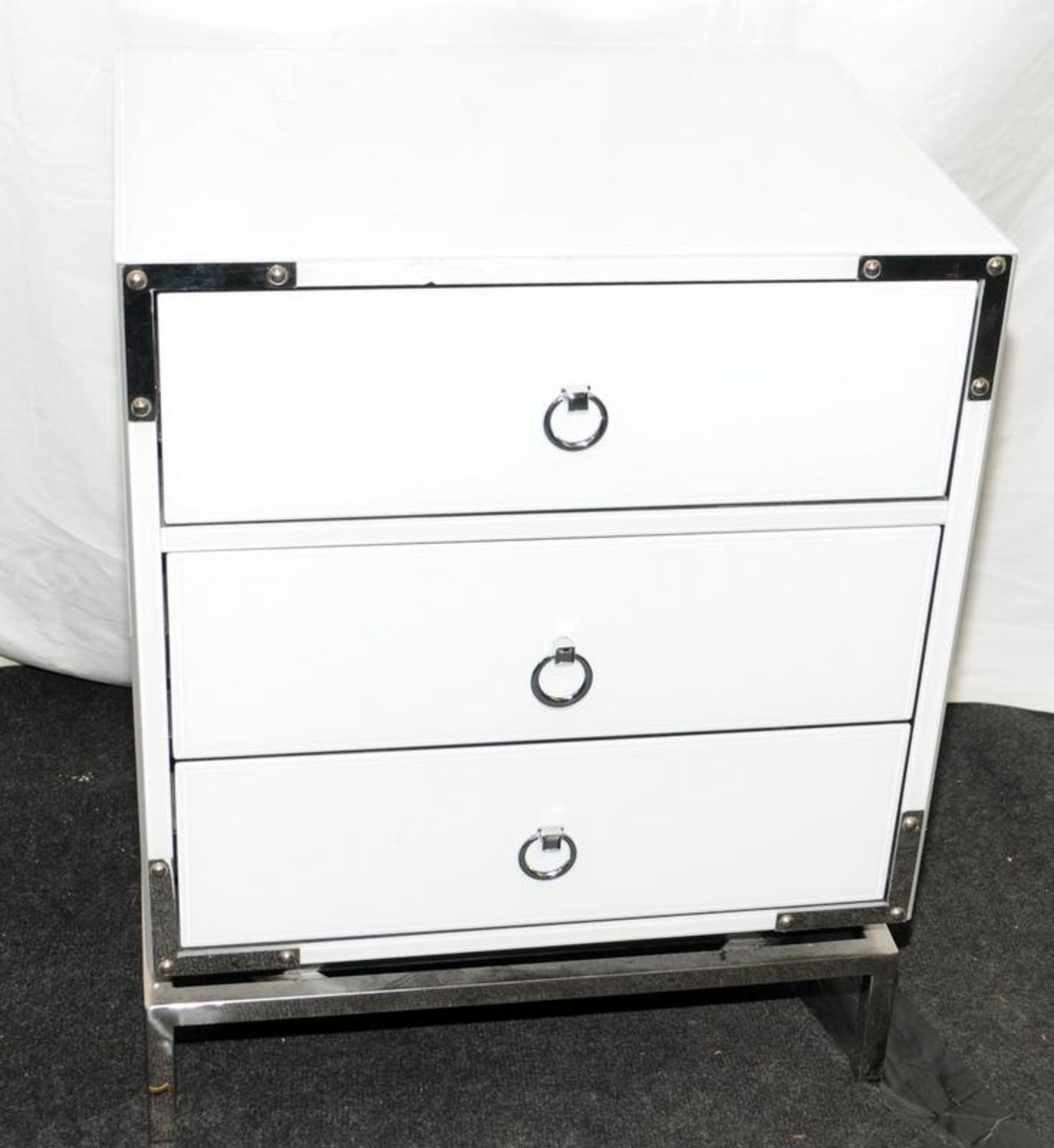 Contemporary white glass three drawer bedside chest on chrome feet with chrome furniture and