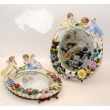 Two antique oval china easel backed mirror frames decorated with flowers, foliage and putti. Some