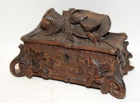 A carved Black Forest casket with hinged lid featuring a hat and basket, with leaf decoration around