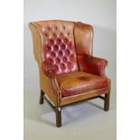 A leather wing armchair with button back and brass stud detail, raised on moulded square form