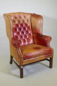 A leather wing armchair with button back and brass stud detail, raised on moulded square form