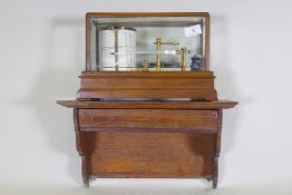 A brass barograph in a glazed oak case with wall bracket fitted with a drawer, glass cracked, drawer