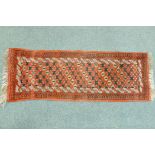 A small hand woven wool village runner with trellis design on a red ground, 140 x 50cm