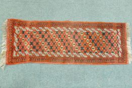 A small hand woven wool village runner with trellis design on a red ground, 140 x 50cm