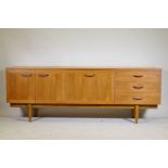 A mid century teak sideboard with two cupboards and three drawers flanking a central fall front,