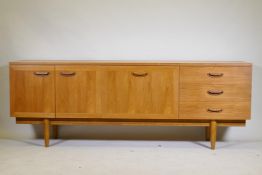 A mid century teak sideboard with two cupboards and three drawers flanking a central fall front,