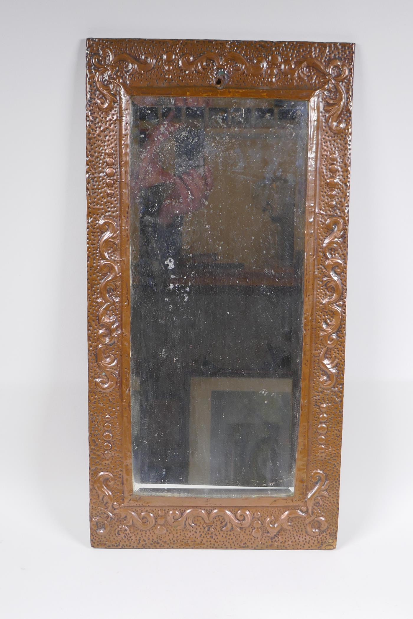 An antique beaten copper wall mirror with repousse swag decoration, 56 x 28cm