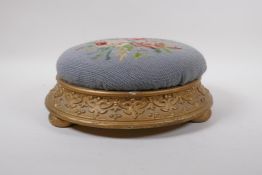 An antique gilt footstool with floral embossed pad, 30cm diameter