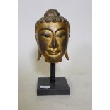 A carved giltwood head of Buddha, mounted on a wood stand, 33cm high