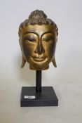 A carved giltwood head of Buddha, mounted on a wood stand, 33cm high