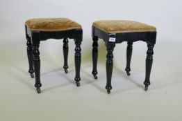 A pair of Victorian ebonised stools, with shaped friezes, raised on turned supports with metal