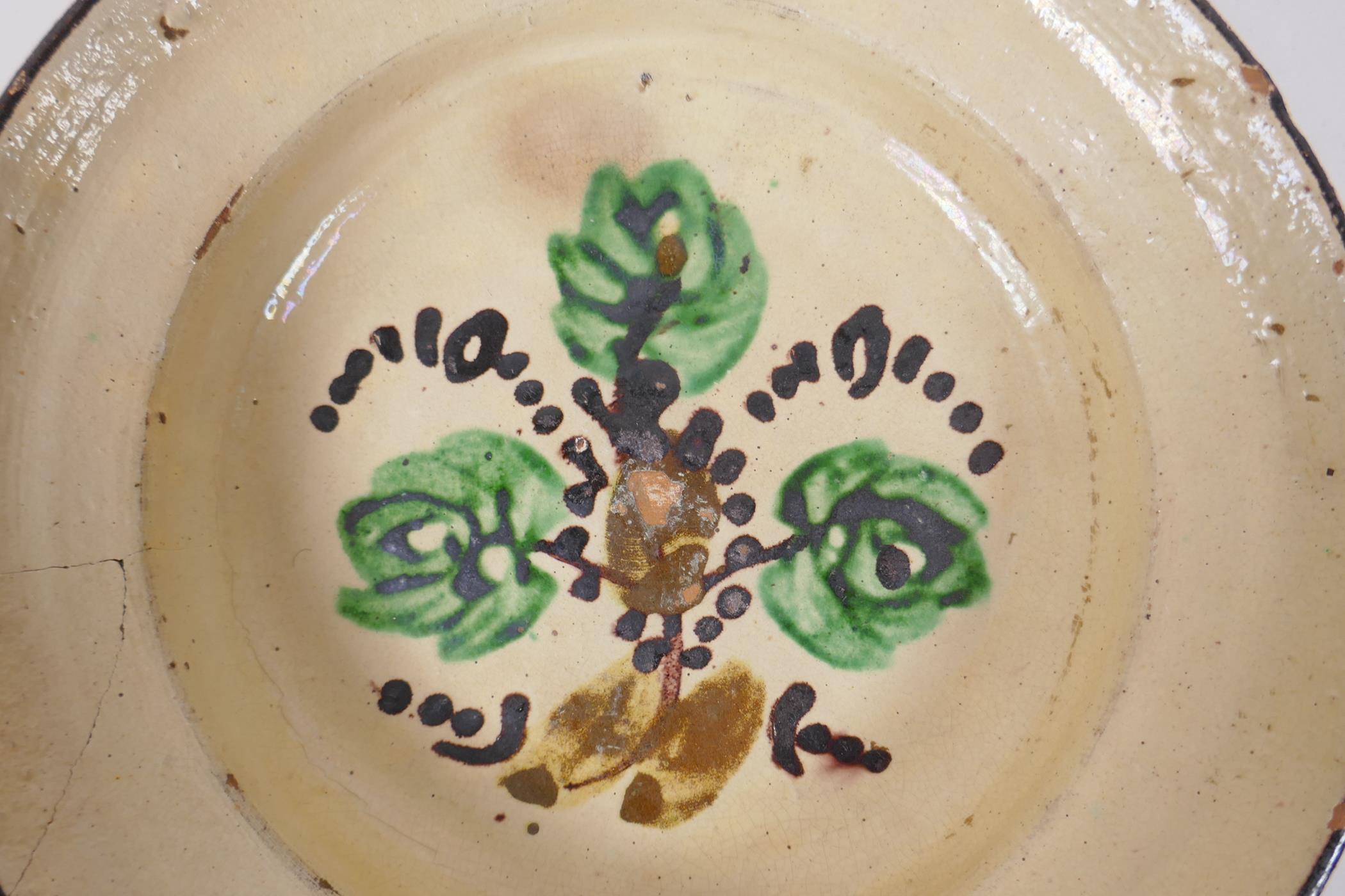 An antique Spanish terracotta dish with a faience glaze and floral decoration, AF repair, 21cm - Image 3 of 6