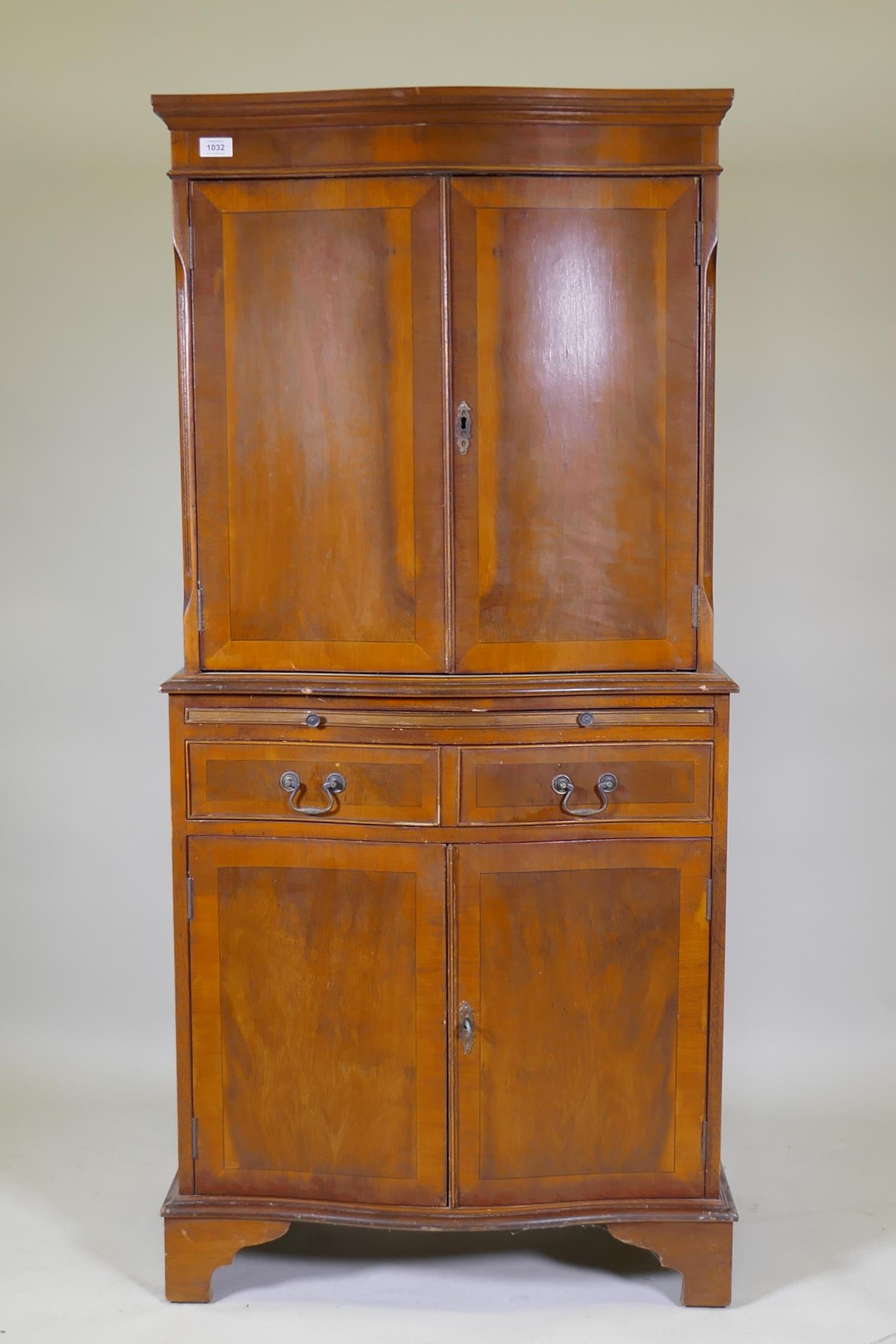 A serpentine front yew wood cocktail cabinet, with two cupboards and mirror back interior,
