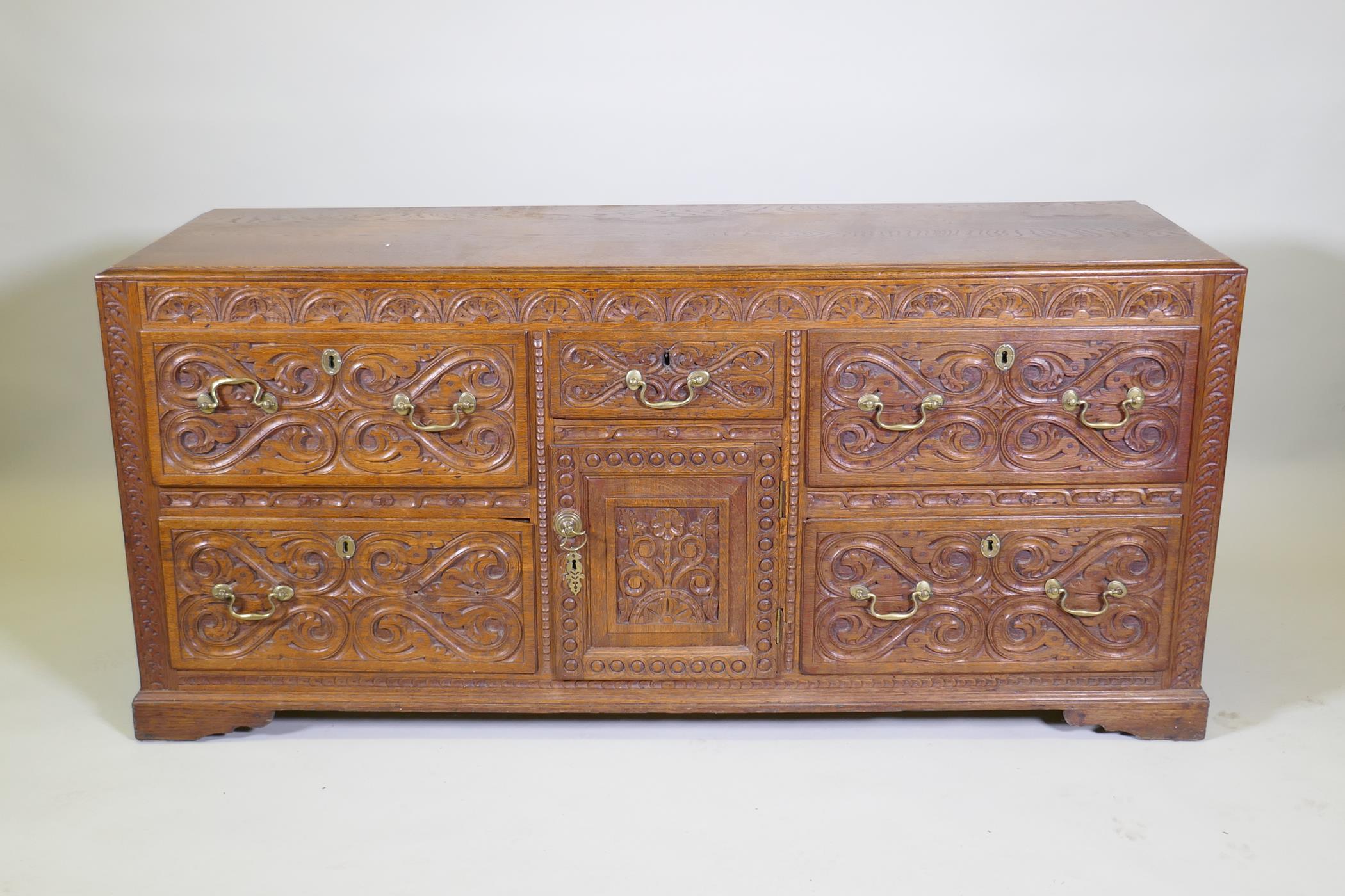 A carved oak sideboard/buffet with five drawers and a single door, with brass swan neck handles,