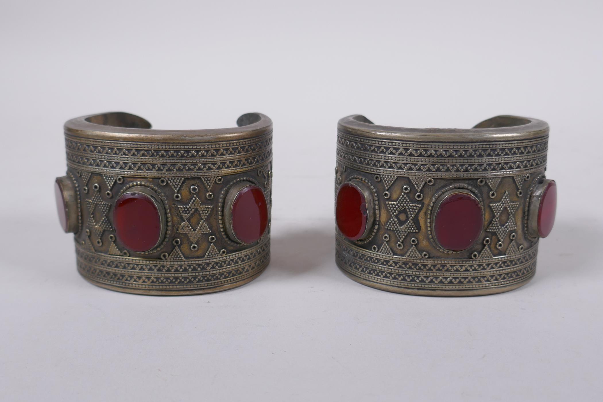 A pair of Turkmen white metal bangles set with red semi precious stones, 8 x 6cm