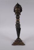 A Tibetan bronze ceremonial phurba and stand, with a wrathful deity mask to handle, 33cm high