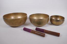 Three Tibetan graduated polished bronze singing bowls, with hammered finish and two wood hammers,