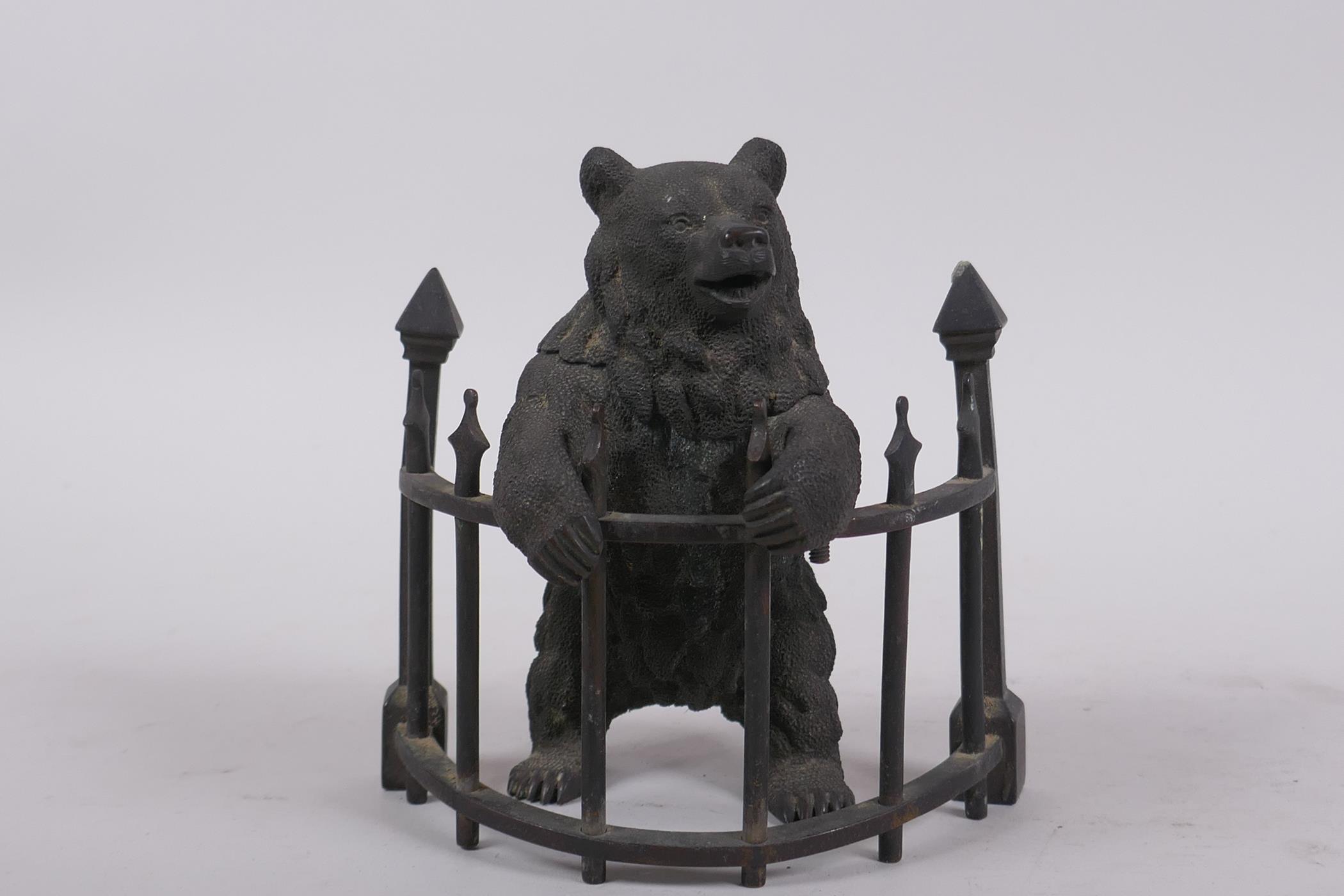 A C19th finely cast patinated bronze inkwell in the form of a bear behind railings, 12cm high