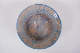 An Islamic terracotta bowl decorated with figures seated by a lotus flower, with a turquoise rim,