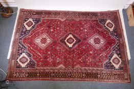 A hand woven red ground Persian carpet with a unique medallion design and chocolate brown borders,